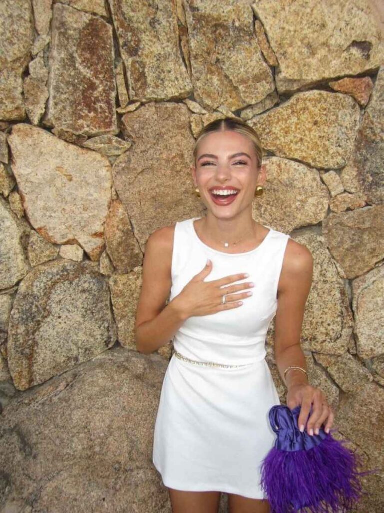 ragazza bionda con abito bianco e borsa viola con piume