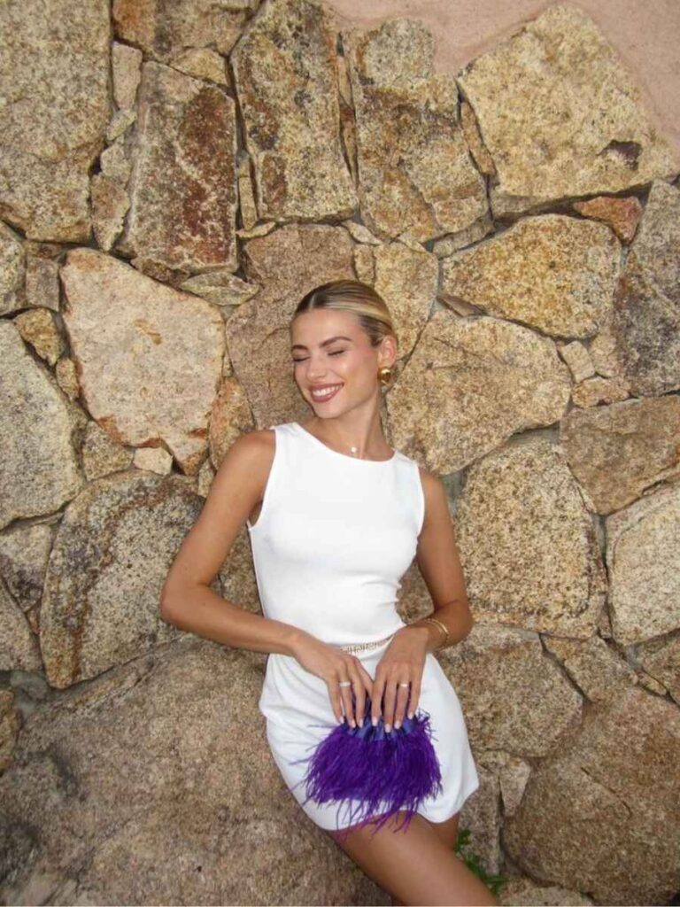 ragazza bionda con abito bianco e borsa viola con piume